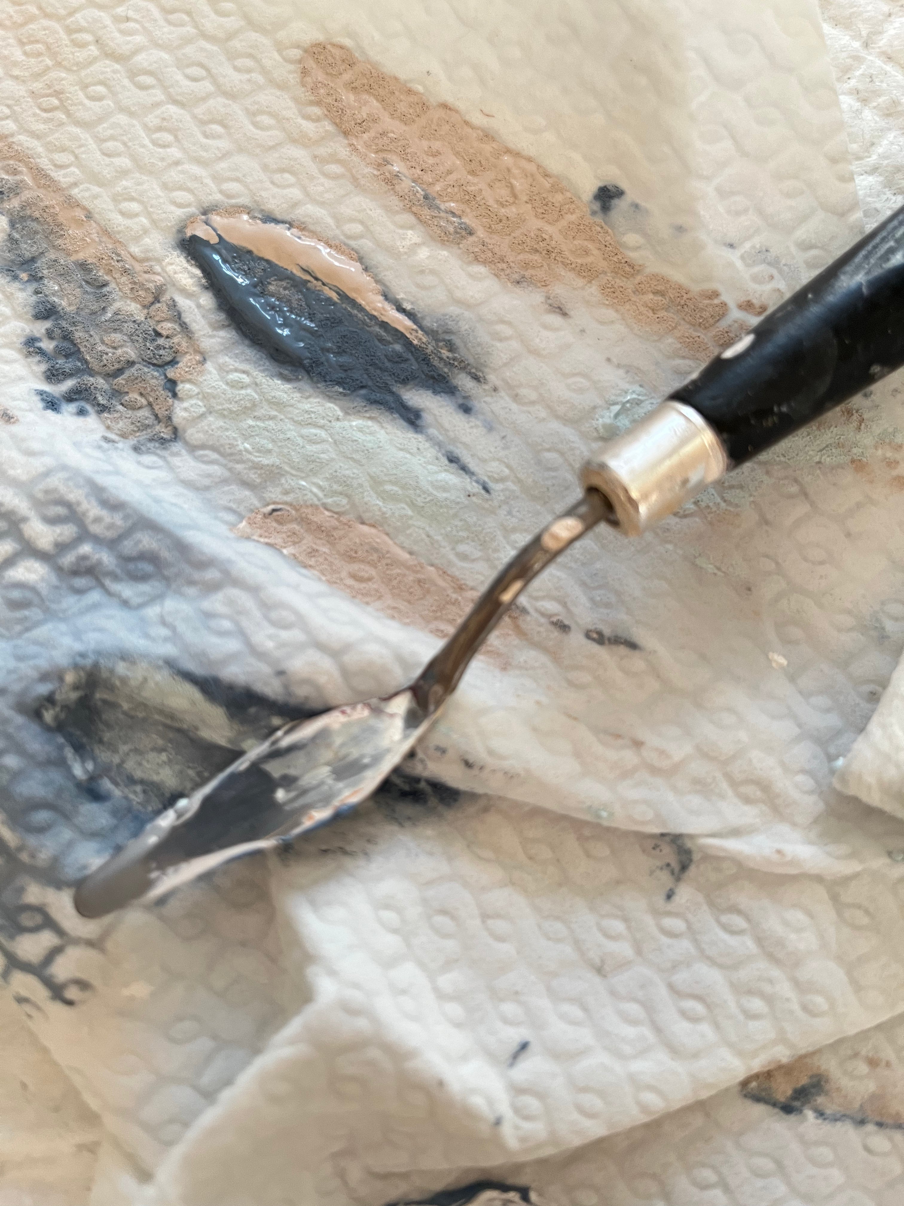 Detailfoto kleiner Spachtel und grau blau und nude Töne auf einem Tuch.