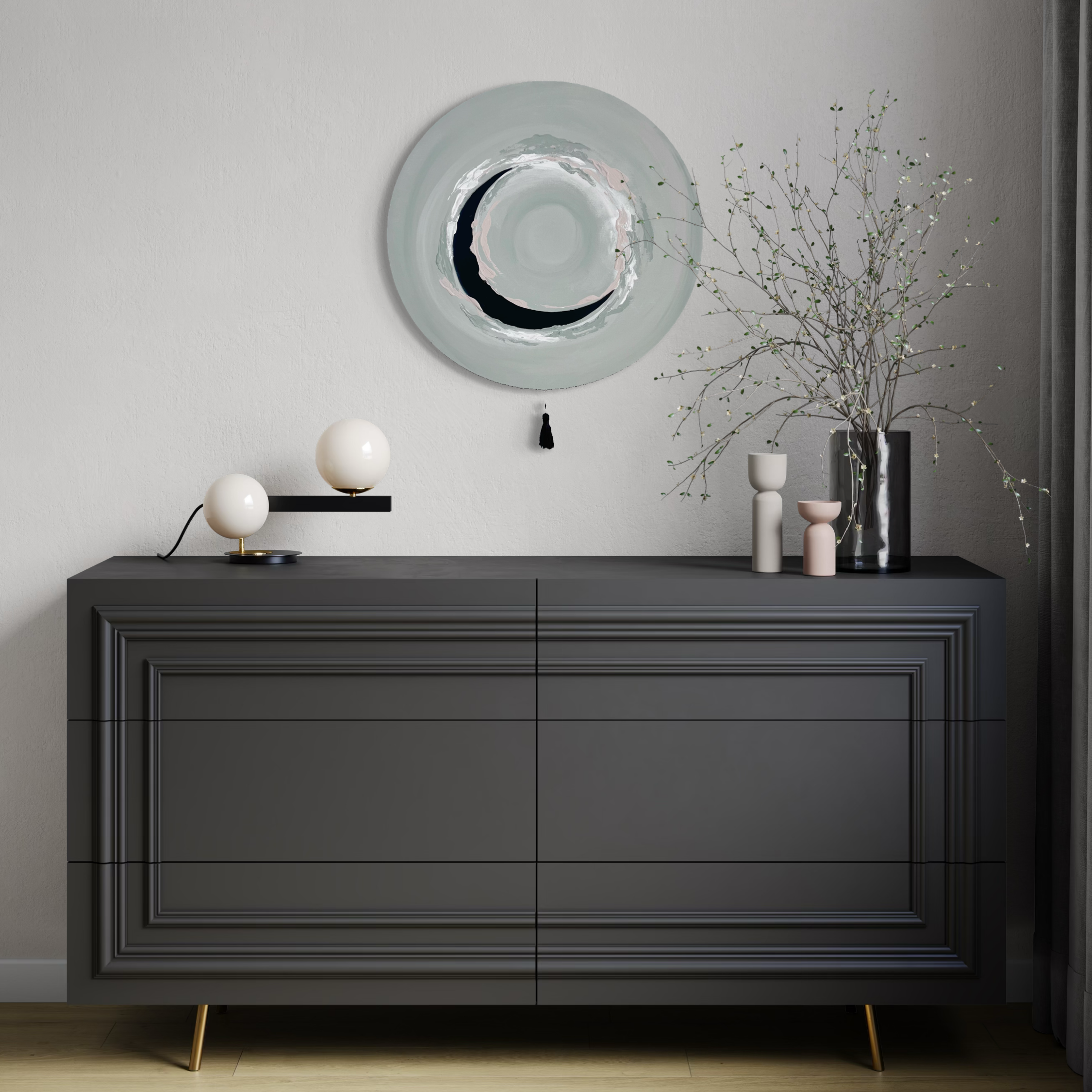 Das Kunstwerk "natural circle". Moderne Wabi Sabi Kunst mit daoistischer Seele von Nadine Elsner. 60cm im Durchmesser. Zarte gedeckte grün Töne mit weichem Kunstleder im Halbkreis in der Mitte des Bildes. Sanfter Abschluss mit einer schwarzen Quaste. Das Bild ergänzt einen dunkel gehaltenen Raum über einer anthrazitfarbenen Kommode. Es ist, als bringt es optisch den Zyklus der Jahreszeiten und harmoniert so schön mit den zarten Frühlingszweigen.