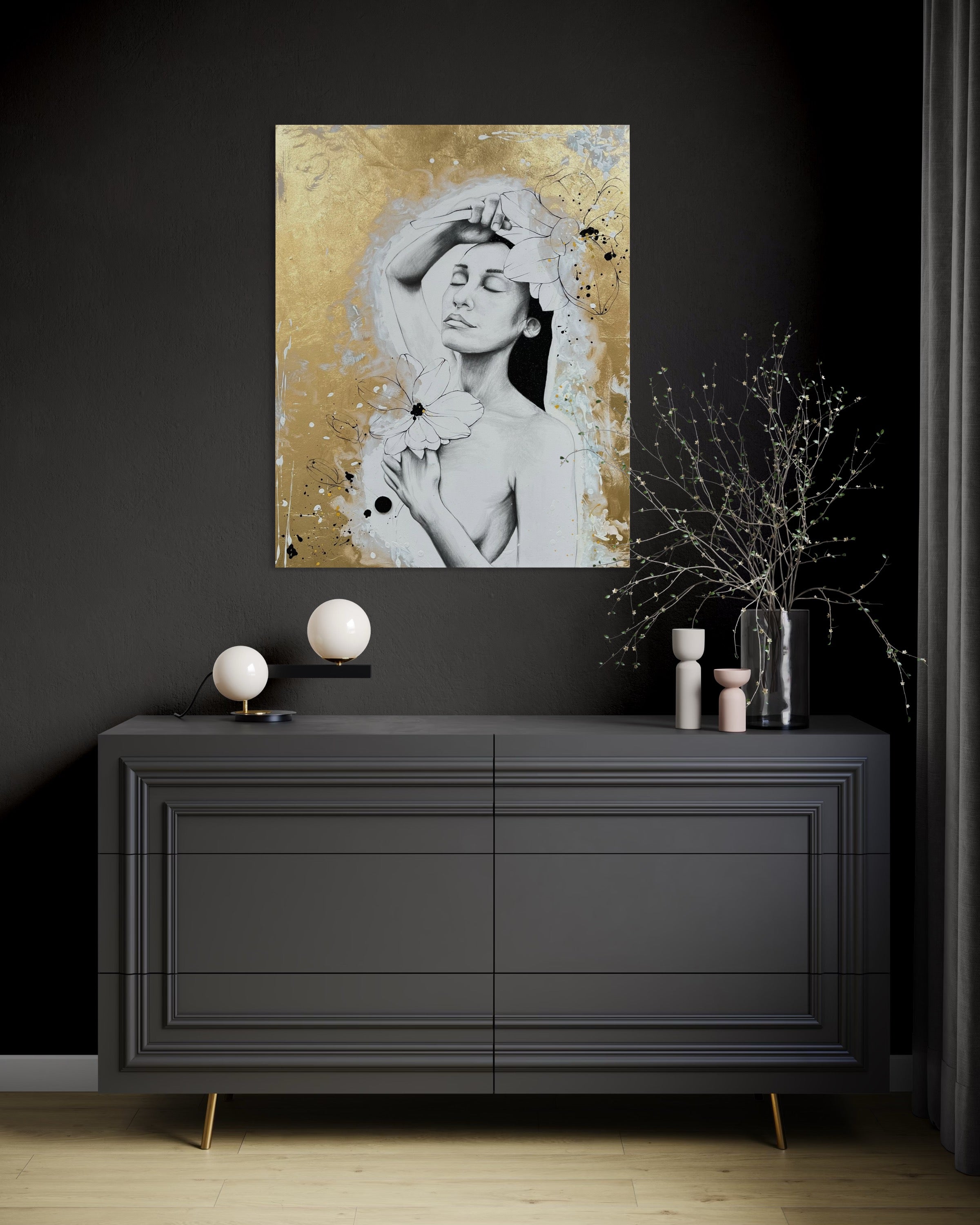 Das Werk hängt in einem dunkel gehaltenen Raum an einer schwarzen Wand. Unter dem Bild steht eine Kommode in Anthrazit mit goldenen Füßen. Die Deko auf der Kommode ist kontrastreich hell und dunkel mit goldenen Akzenten.