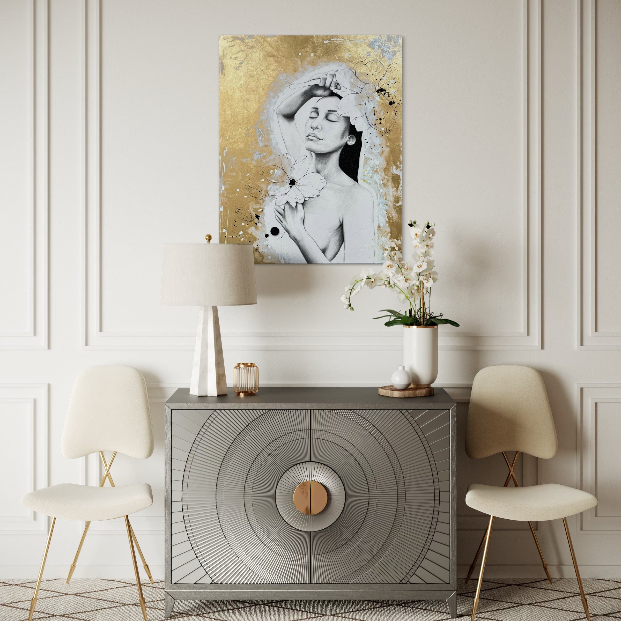Das Werk hängt über einer hellgrauen Kommode an einer beigen Wand. Rechts und links neben der Kommode stehen 2 beige Stühle. Überall gibt es goldenen und rostgoldene Details. Alles harmoniert wundervoll mit dem Werk.