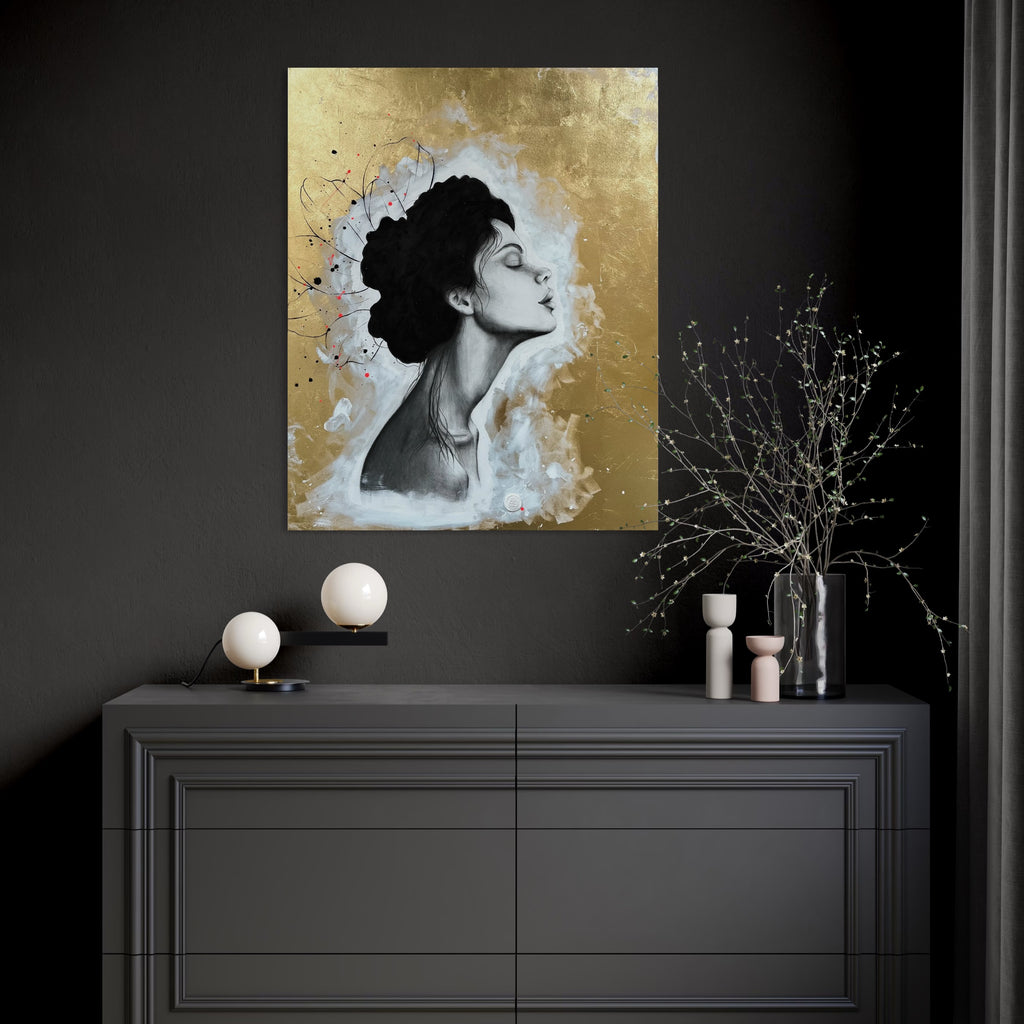 Das Werk hängt in einem modern dunkel gehaltenen Raum über einer dunklen Kommode. Auf der Kommode gibt es Deko mit hellen und goldenen Akzenten.